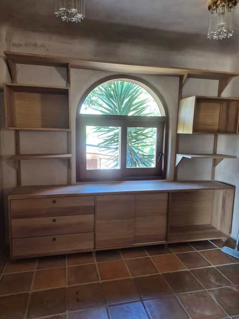 Mueble a medida con cajones, puertas y estantes de madera alrededor de una ventana en arco, Ibiza