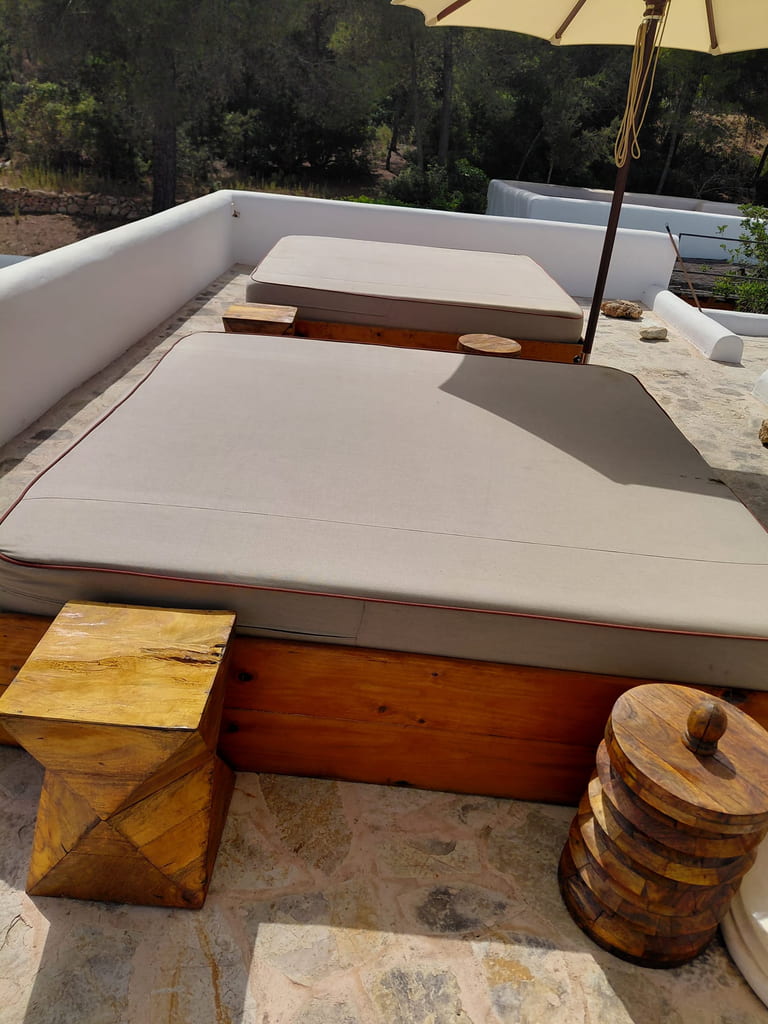 Camas de exterior con base de madera y mesitas de tronco en una terraza de Ibiza