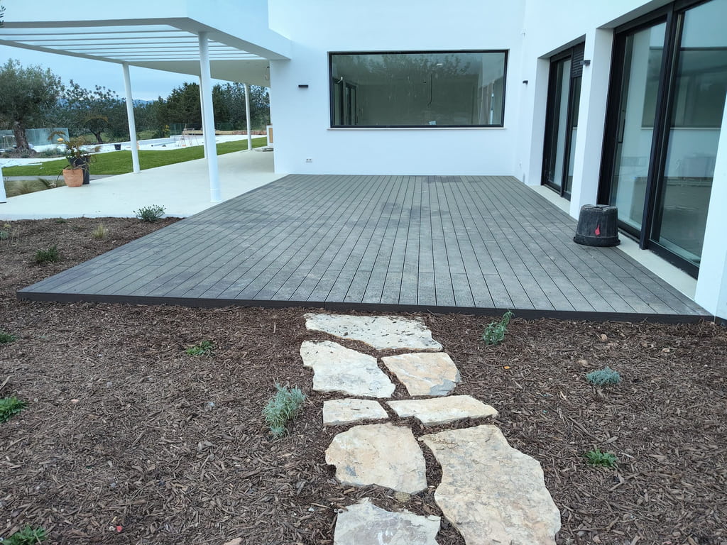 Terraza exterior con tarima composite gris junto a villa moderna con jardín, Ibiza