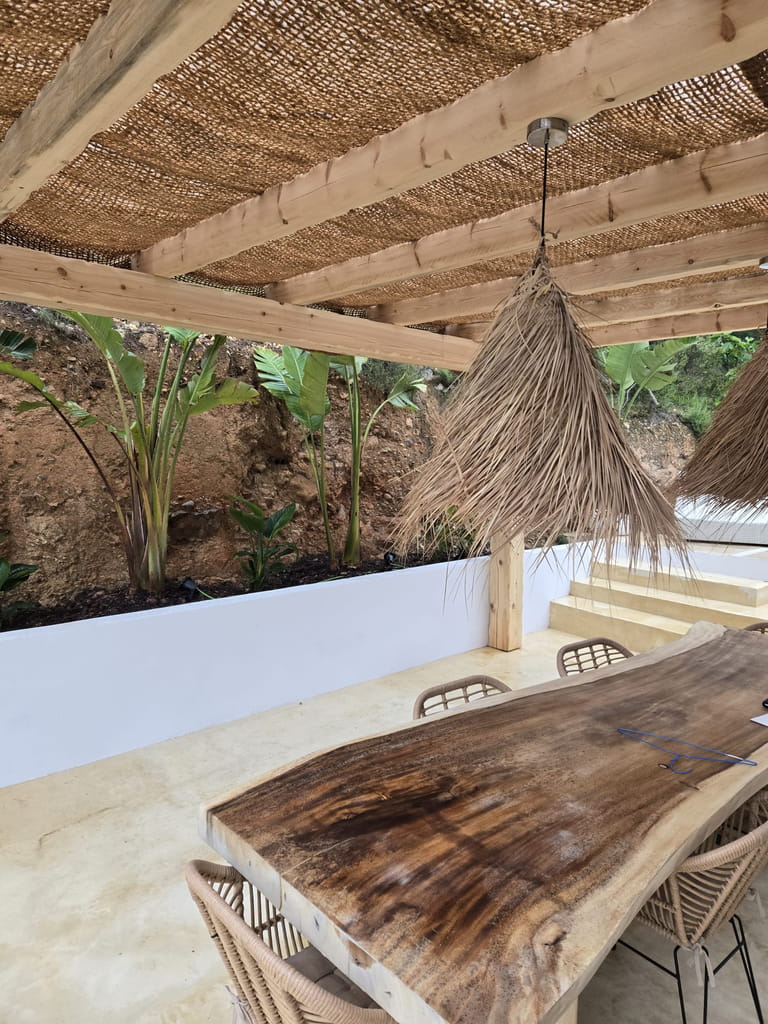 Pérgola de madera con cubierta de brezo sobre comedor exterior con mesa de madera natural, Ibiza