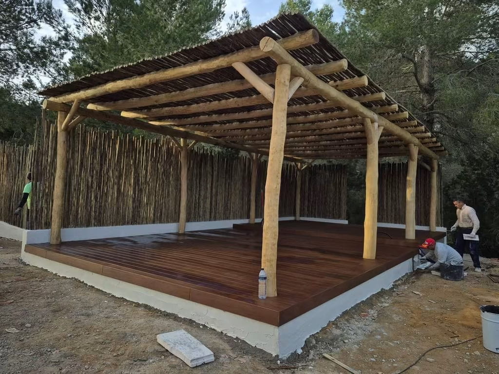 Pérgola de troncos de madera con cubierta de brezo y suelo de tarima, en construcción, Ibiza